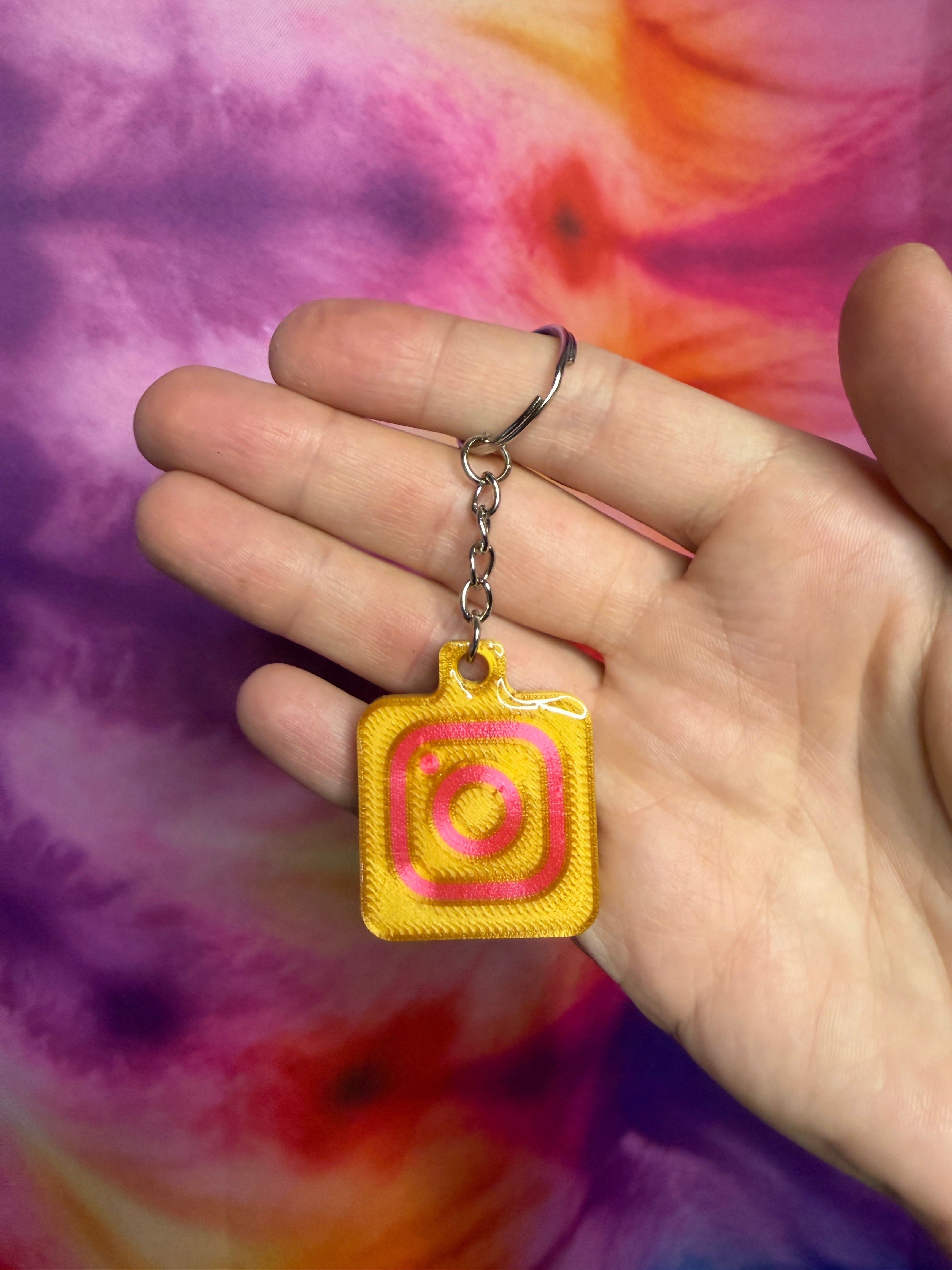 Yellow  gold and pink keychain with a pink center held in a hand against a tie-dye background