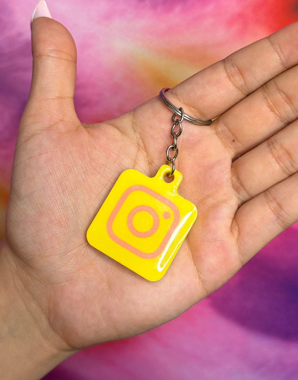 Hand holding a yellow square keychain with a circular design against a tie-dye background