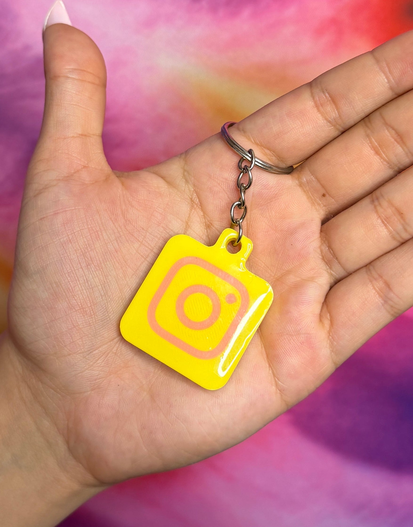 Hand holding a yellow square keychain with a circular design against a tie-dye background