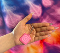 Hand holding a pink keychain with a camera icon against a tie-dye background