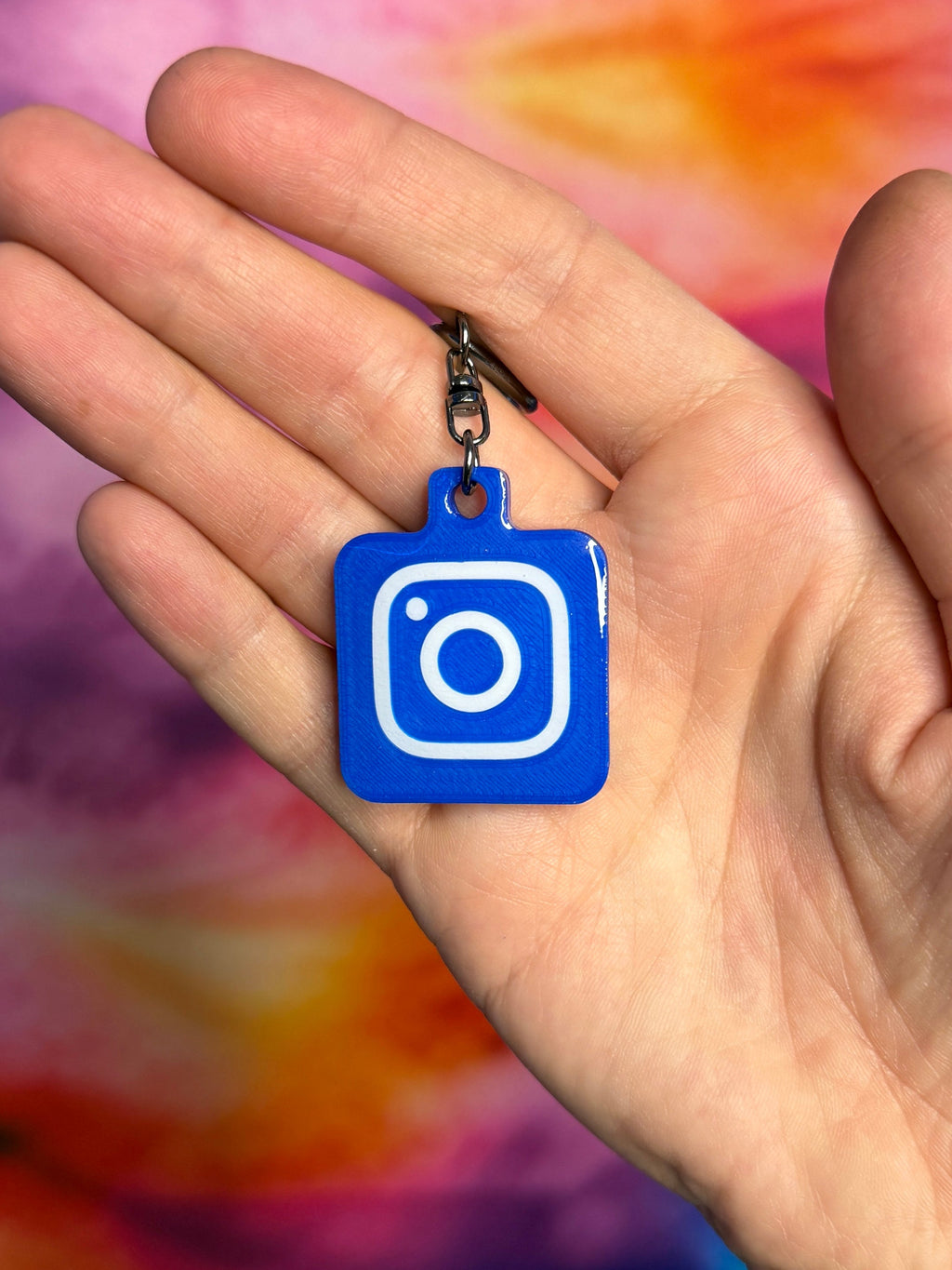 Hand holding a blue Instagram keychain against a tie-dye background