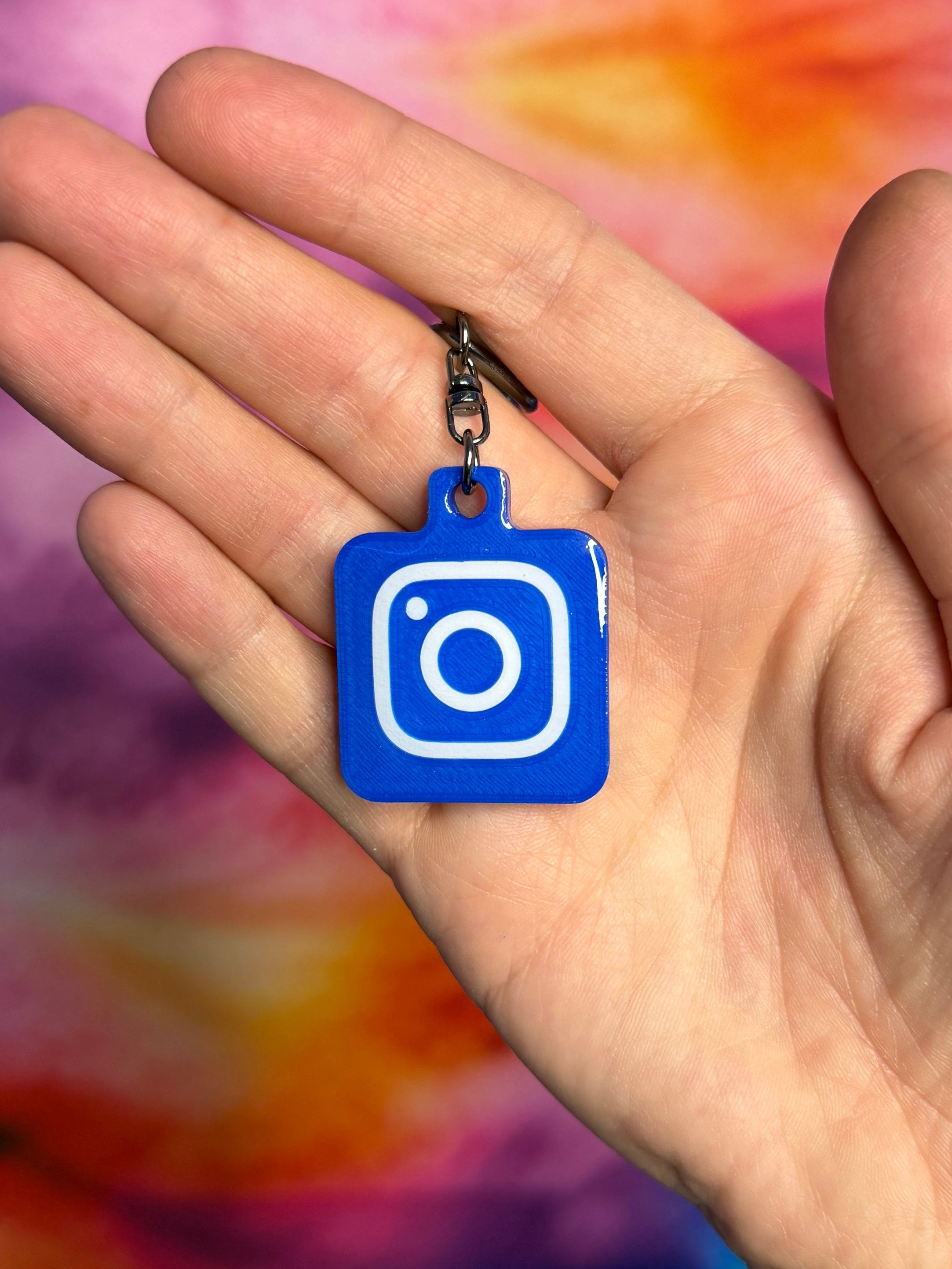 Hand holding a blue Instagram keychain against a tie-dye background