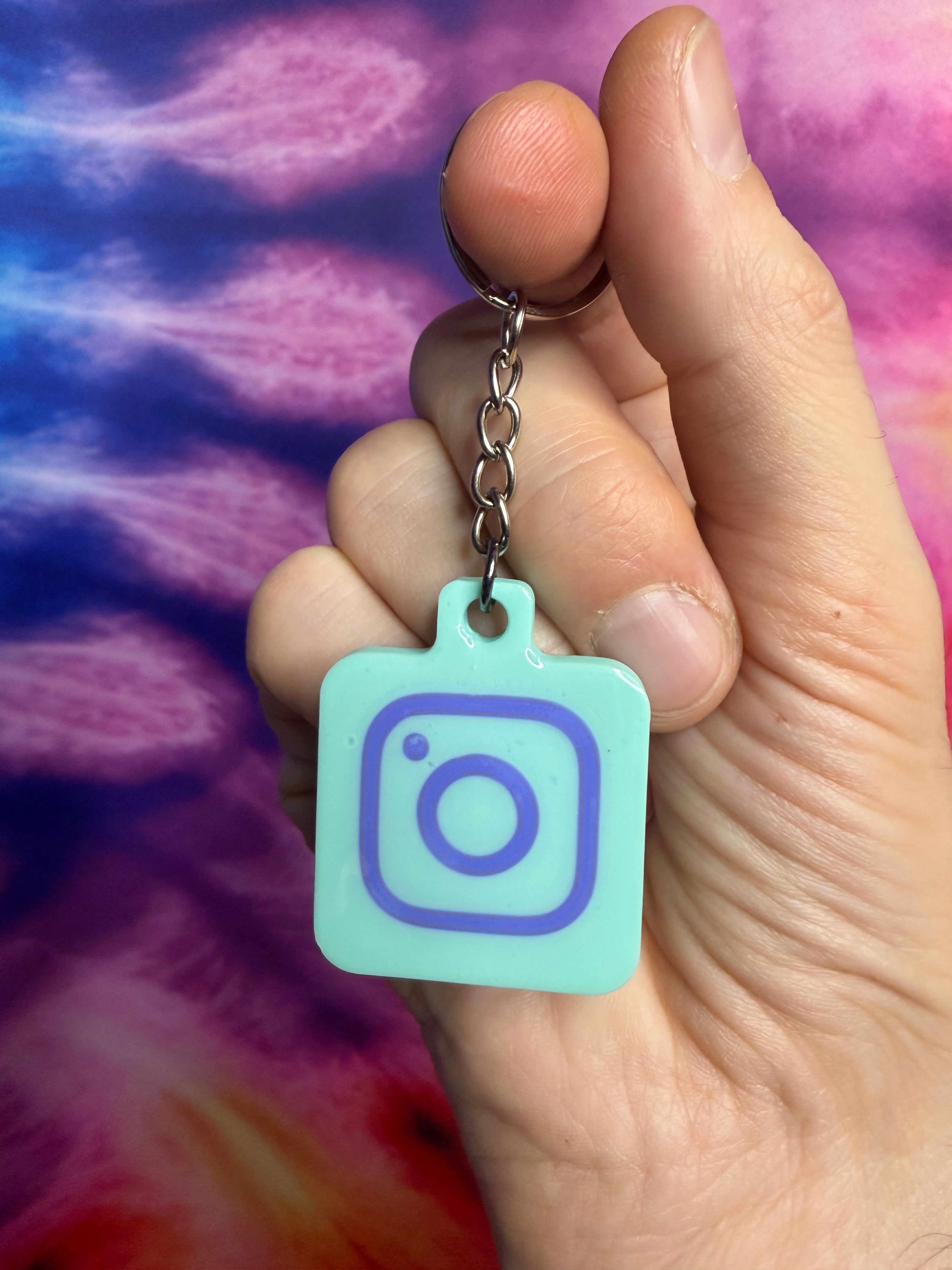 Hand holding a keychain with an Instagram logo against a tie-dye background