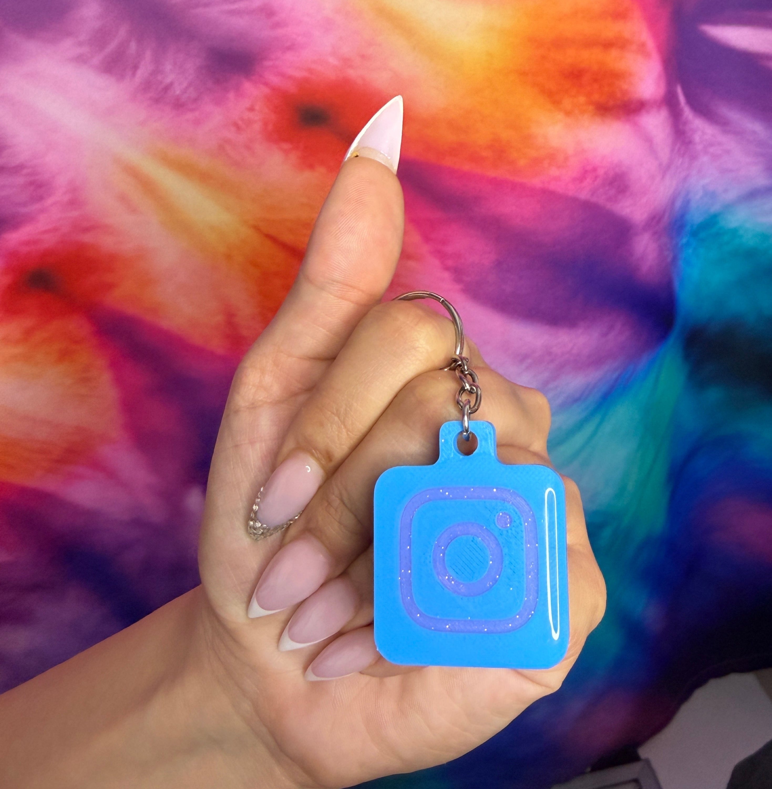 Hand holding a blue keychain with a square design against a tie-dye background