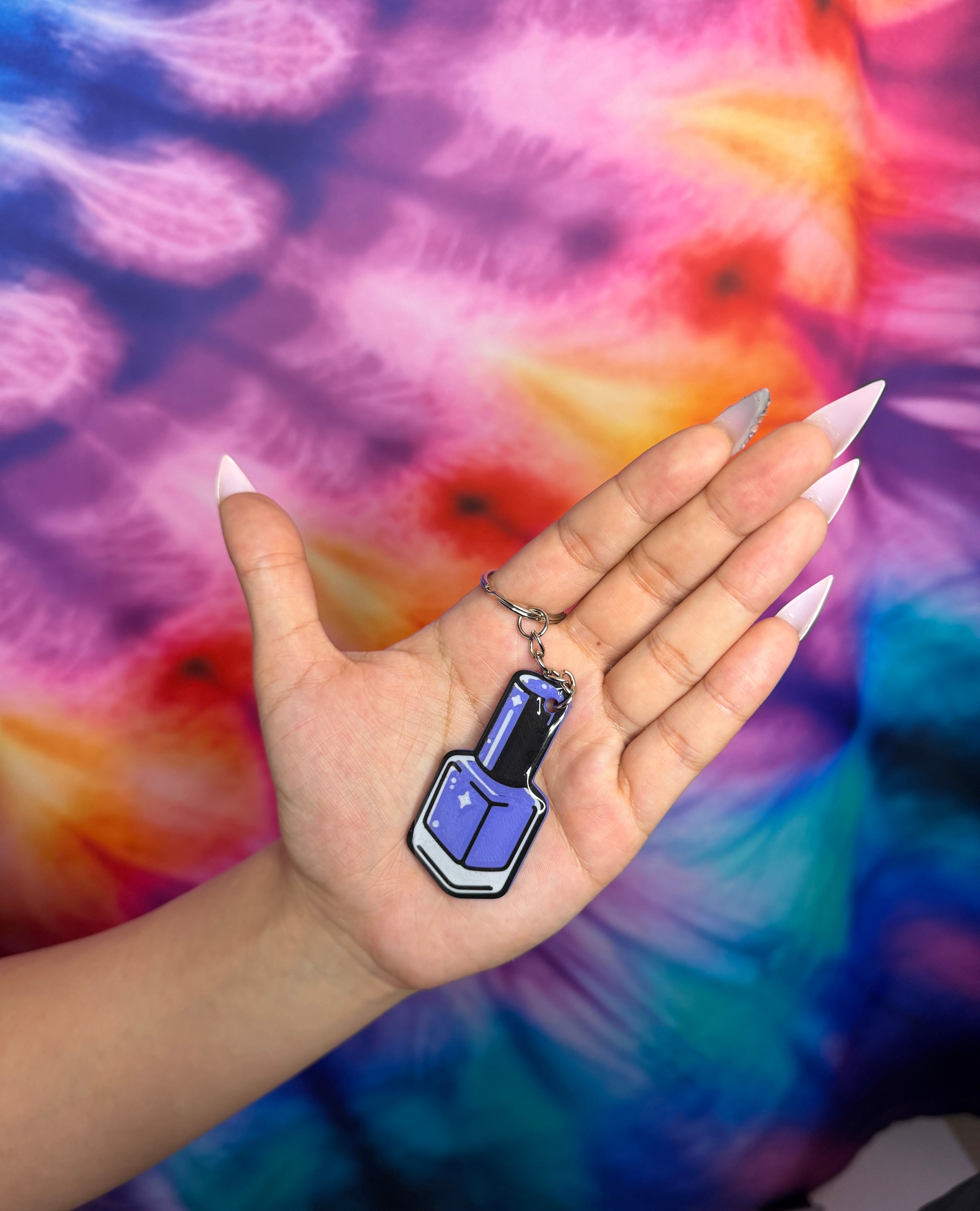 Hand holding a purple nail polish keychain against a tie-dye background