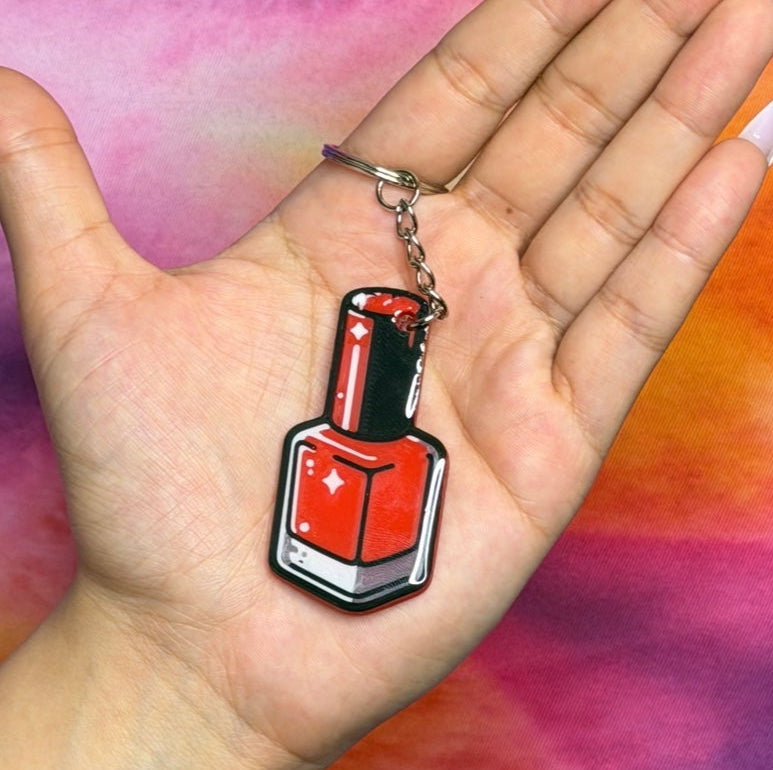 Hand holding a keychain with a nail polish design against a tie-dye background
