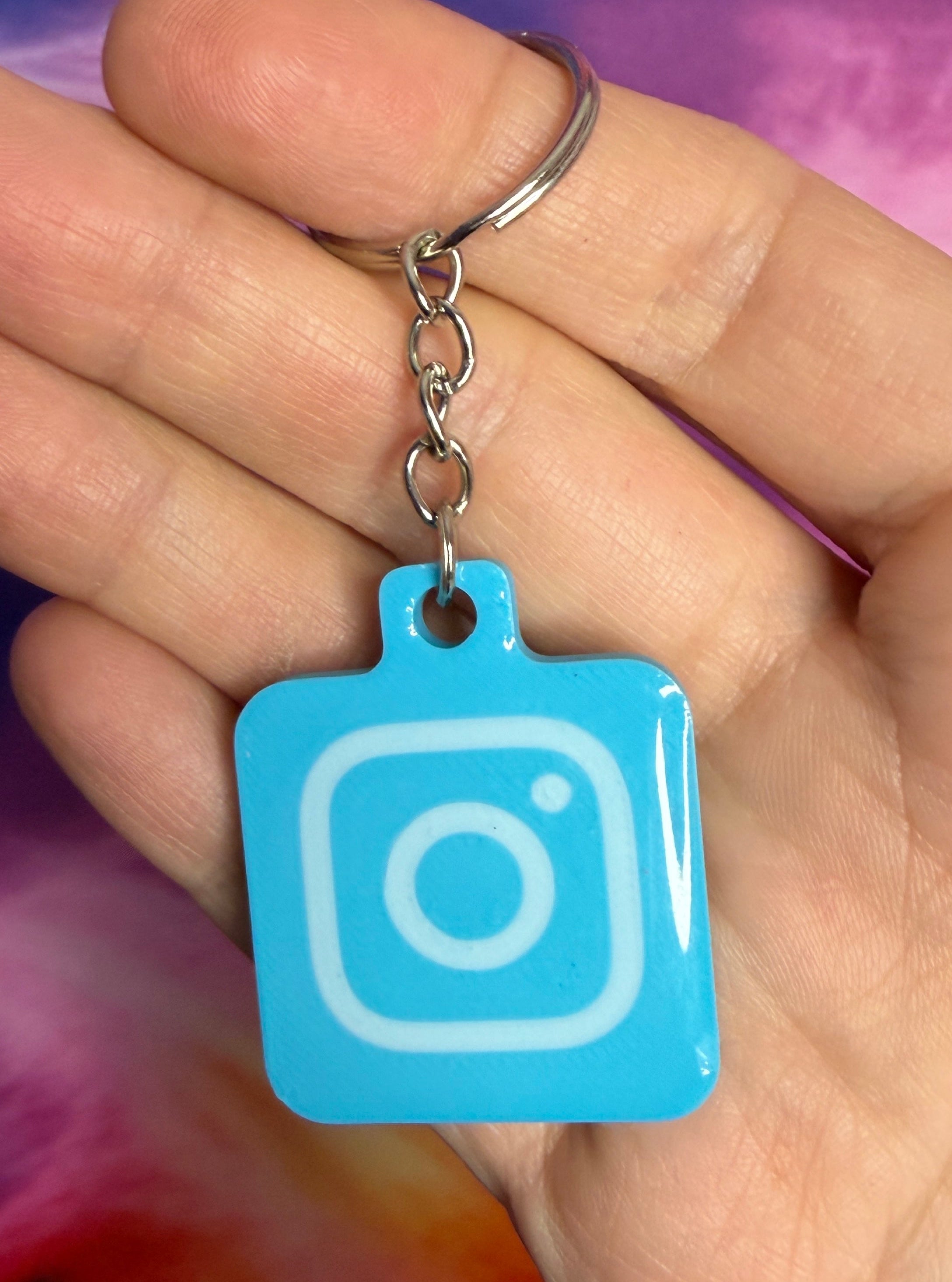 Hand holding a blue Instagram logo keychain against a tie-dye background